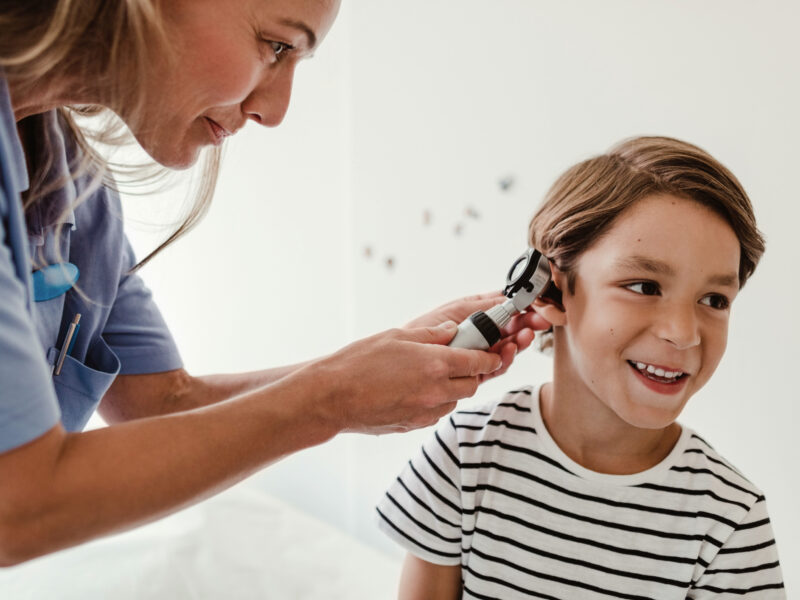 Doctor examining boy's ear with otoscope in medical examination room